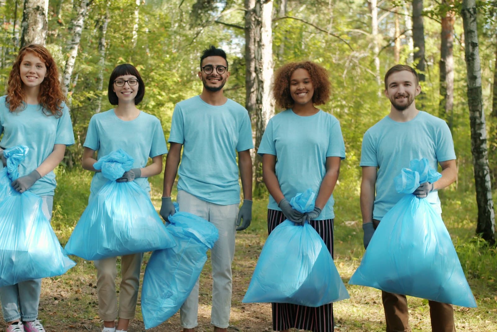 Five volunteers in matching shirts holding full trash bags after a park cleanup