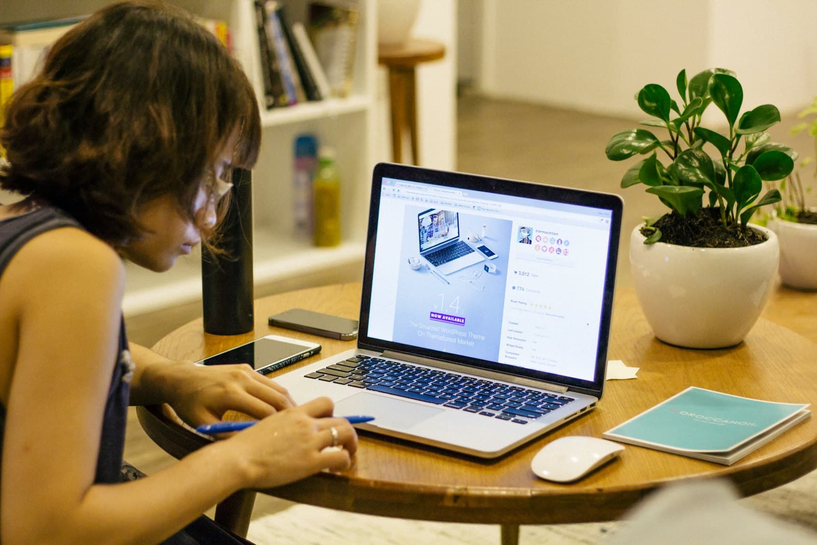 A student working on a laptop at a small desk with a plant and a notebook