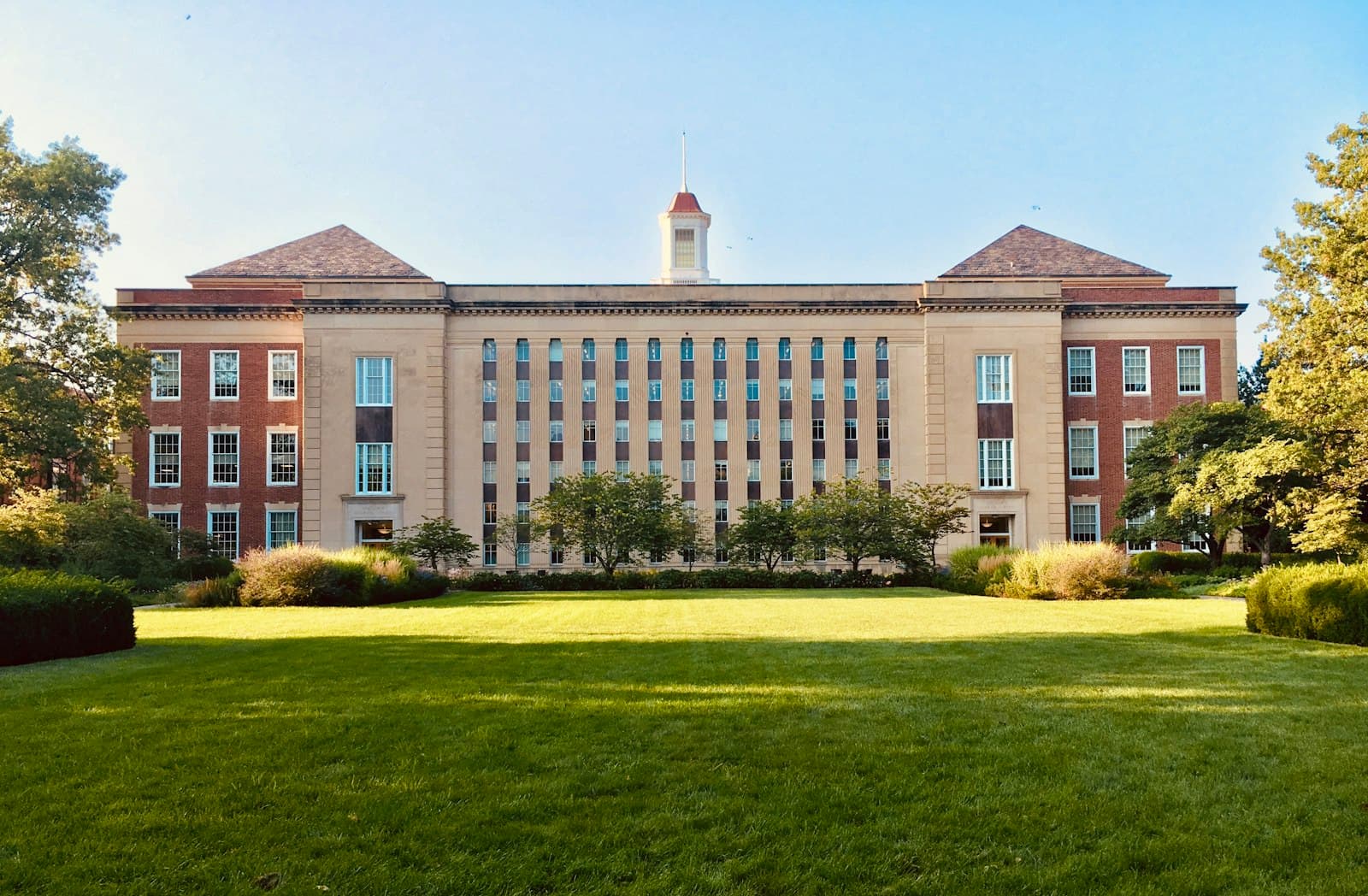 A brick university hall behind a wide green campus lawn