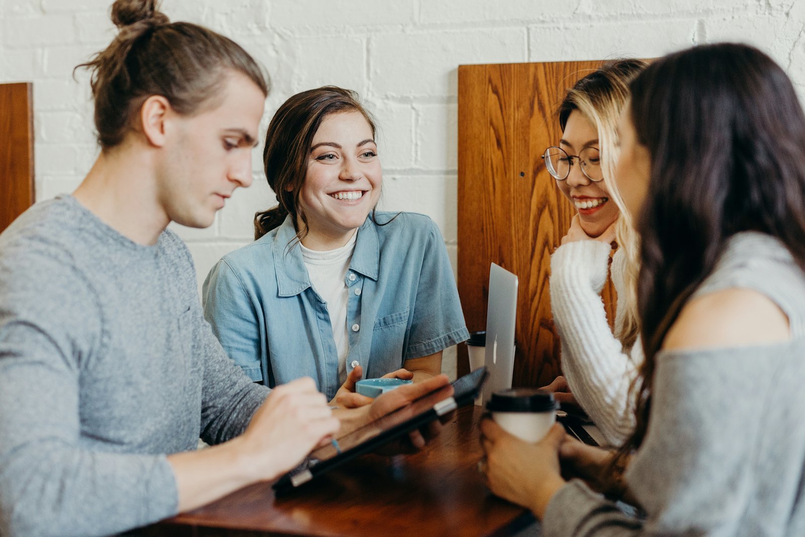 Four young people working together around a table with a tablet and a laptop