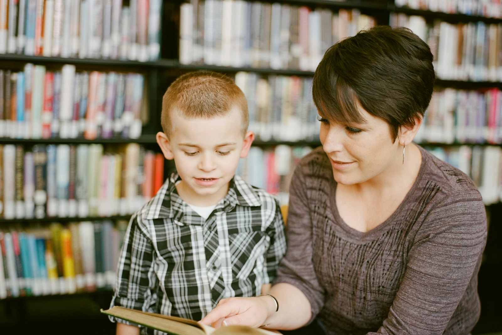 A tutor reading a book with a young student in a library